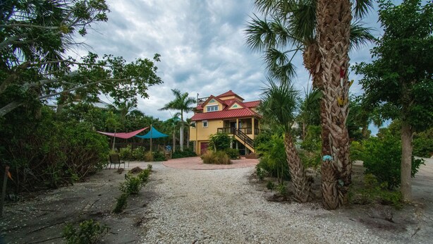 A two-story building with a red roof, surrounded by palm trees and greenery. - The Salty Conch - Luxury Just Steps To The Beach with Private Pool;2 Golf Carts (Captiva)
