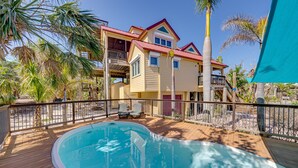 A two-story house with a swimming pool, wooden deck, and a fenced area with palm trees. - The Salty Conch - Luxury Just Steps To The Beach with Private Pool;2 Golf Carts (Captiva)