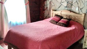 A bed with a pink bedspread in a room with a stone wall and wooden beams. - Sna Cabins (San Cristóbal de las Casas)