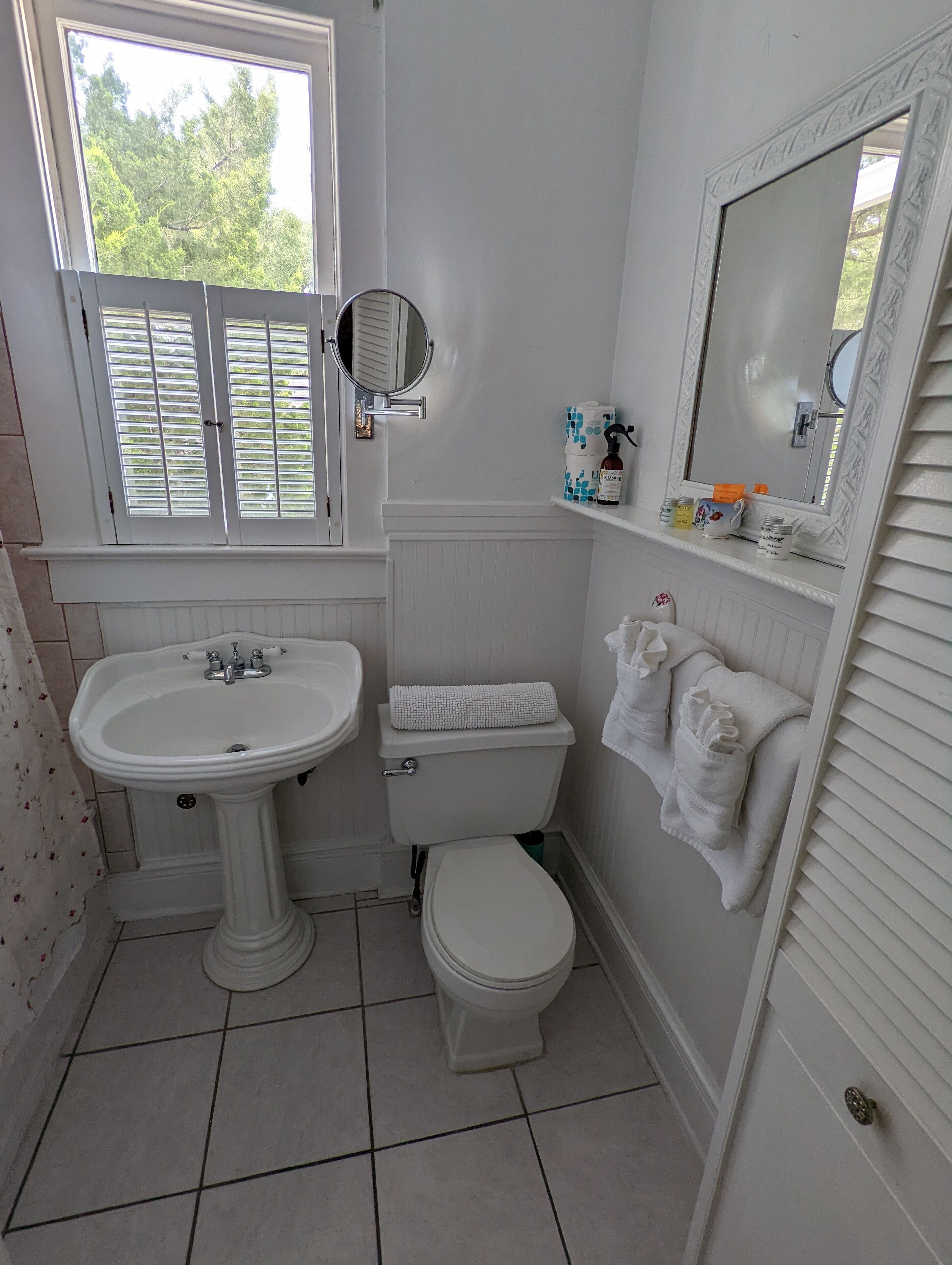 Une salle de bain avec un lavabo sur colonne, des toilettes et une fenêtre avec des volets.
