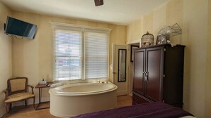 A bedroom with a large bed, a bathtub, a wardrobe, and a television on the wall. - Old Powder House Inn (St. Augustine)