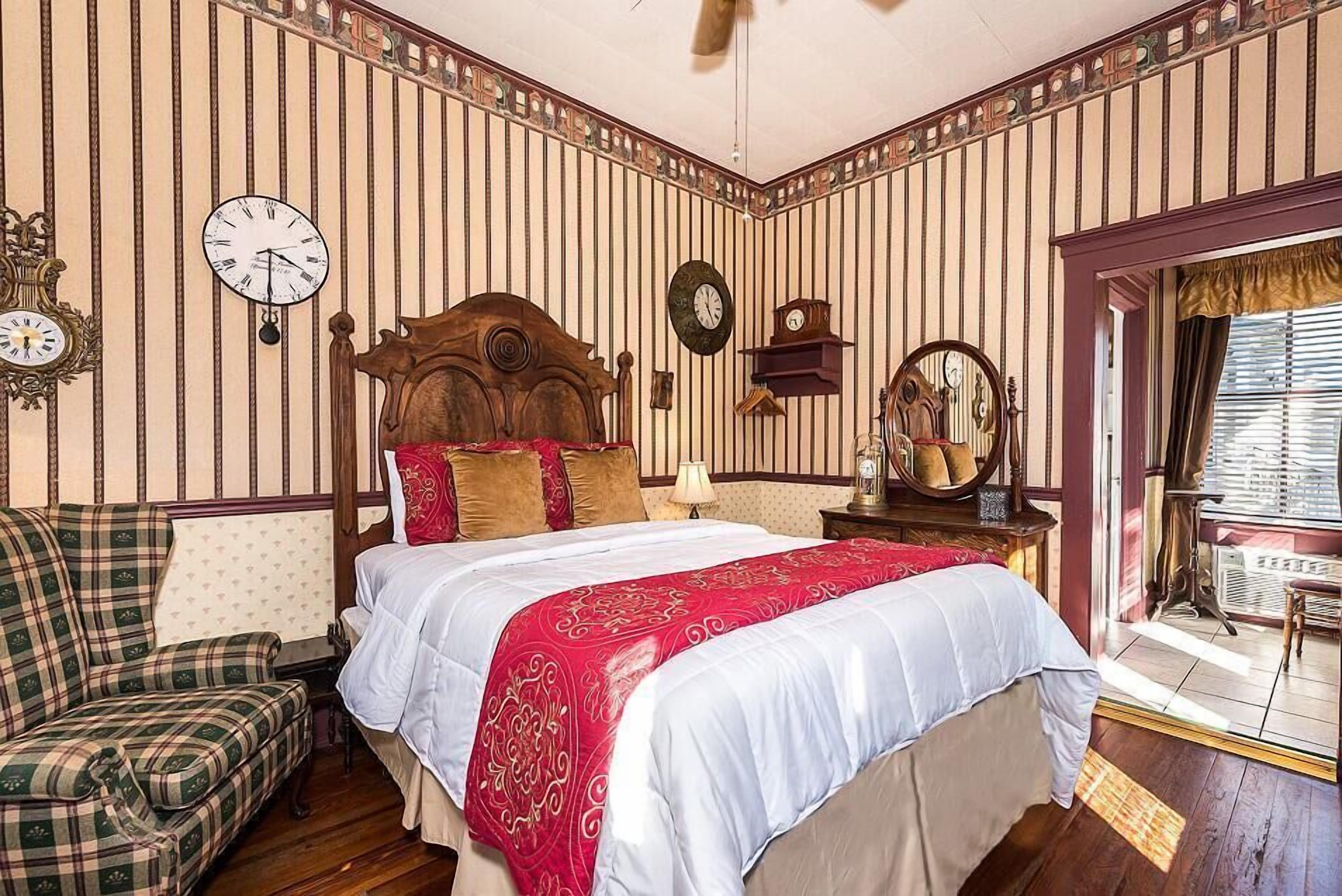 A room with a bed, a wooden headboard, a clock, and a window with blinds.