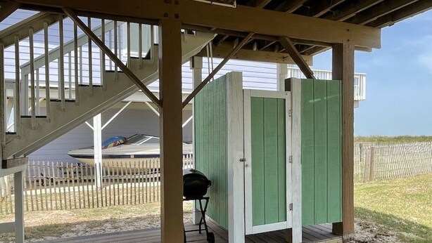 Een overdekt buitengebied met een houten terras, een barbecue en een groene constructie met witte deuren.