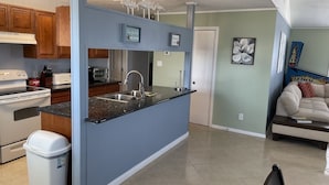 Een moderne keuken met een blauw eiland, roestvrijstalen apparatuur en een zithoek met een bank en salontafel.