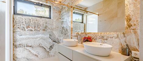 A modern bathroom with two large white sinks, a large mirror, and a window.