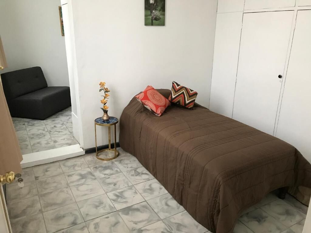 A bedroom with a bed, a small table with a vase, and a grey sofa in the corner.