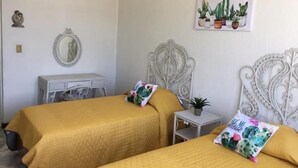 Ein Zimmer mit zwei Betten, einem Schreibtisch und einem kleinen Tisch mit einer Pflanze.