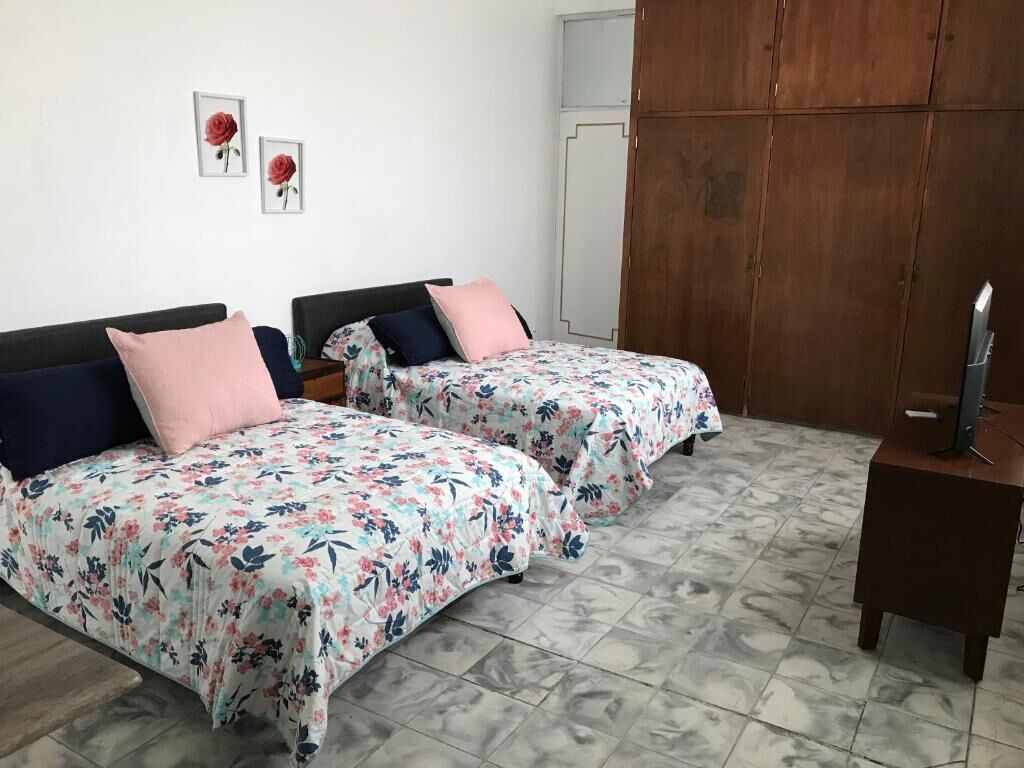 A room with two beds, each with floral bedding and a wooden headboard. There is a wardrobe and a small table with a television.