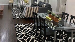 A modern living room with a dining area, featuring a glass table, black chairs, a striped sofa, and a ceiling fan. -  Southern Comfort in Convenient Quiet Neighborhood w/hot tub (San Antonio)