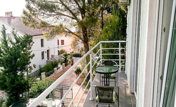 Varanda com mesa e cadeiras, vista para uma rua com edifícios e árvores.