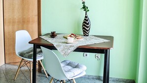 Un coin repas avec une table dressée pour deux personnes, un vase rempli de fleurs et un tableau représentant des figues accroché au mur.
