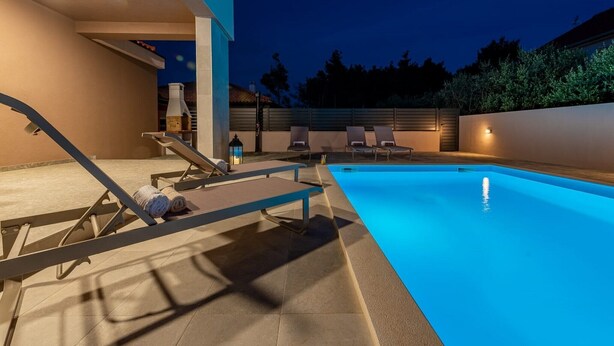 An outdoor swimming pool area with lounge chairs and a barbecue grill.
