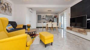 A modern living room with a yellow sofa, a TV, and a kitchen in the background.
