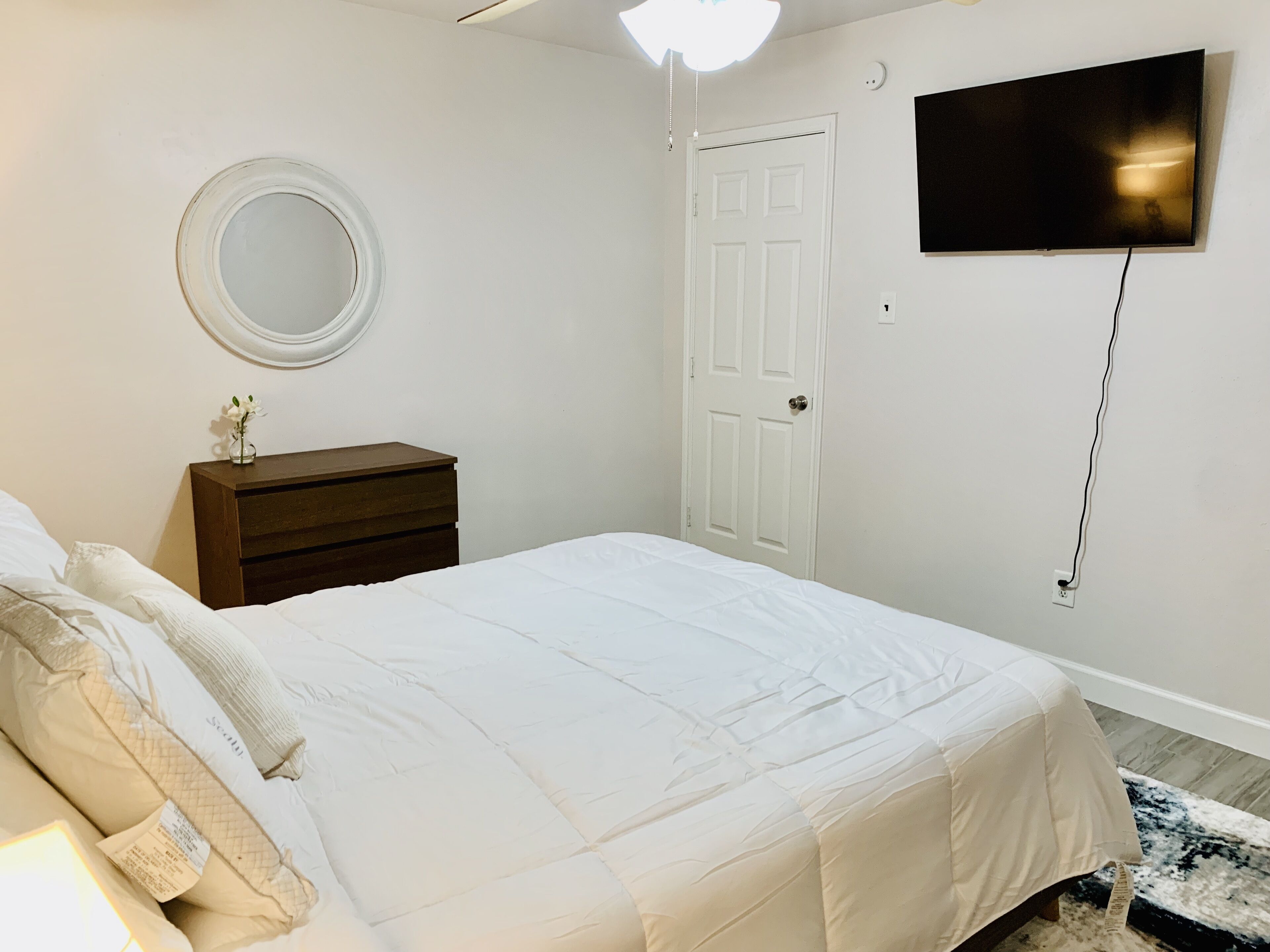 A bedroom with a bed, a dresser, a mirror, a door, and a TV mounted on the wall.