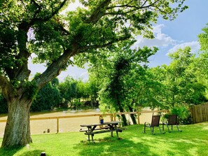 A picnic area with a table and chairs, a large tree, and a view of a river. - Mayfield @ Oyster Creek - WORLD CUP (Sugar Land)