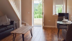 A spacious room with a wooden floor, a black leather sofa, a dining table with chairs, and a staircase. - 1 bedroom accommodation in Aberfoyle (Aberfoyle)