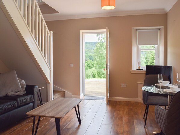 A spacious room with a wooden floor, a black leather sofa, a dining table with chairs, and a staircase. - 1 bedroom accommodation in Aberfoyle (Aberfoyle)