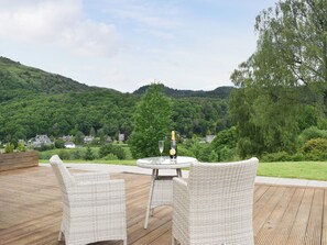 A wicker outdoor seating area with a table and chairs overlooking a lush green landscape and distant houses. - 1 bedroom accommodation in Aberfoyle (Aberfoyle)