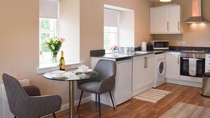 A modern kitchen with a dining area, including a table with chairs, a washing machine, and a microwave. - 1 bedroom accommodation in Aberfoyle (Aberfoyle)