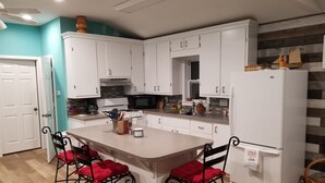 A kitchen with white cabinets, a central island with red cushioned chairs, a refrigerator, and a microwave. - 4 Season newly remodeled all sport lake cottage w/ nearby golfing & snowmobiling (Alto)