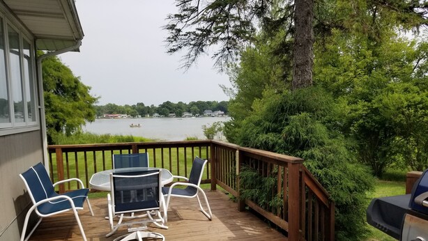 A wooden deck with a table and chairs, overlooking a lake with boats. - 4 Season newly remodeled all sport lake cottage w/ nearby golfing & snowmobiling (Alto)