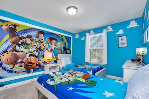 A bedroom with a vibrant blue wall, a large mural of animated characters, and a bed with a blue and white star-patterned bedspread.