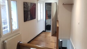 A bedroom with a wooden bed, white bedding, a radiator, and a window. - Atypical apartment house (Annonay)