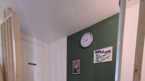 A hallway with a green wall, a clock, and two framed pictures. - Atypical apartment house (Annonay)