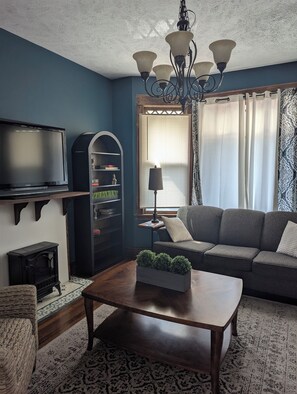 Uma sala de estar com sofá, mesa de centro, televisão, estante e abajur decorativo.