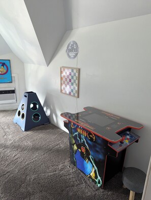 Um quarto com uma mesa de jogos com tema Mortal Kombat, um jogo de tabuleiro quadriculado e um pôster na parede.