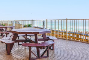 A wooden picnic table and benches on a tiled patio with a view of the ocean.