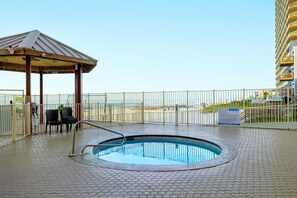 A rooftop pool with a wooden gazebo, hexagonal tiled floor, and a view of a high-rise building in the background.