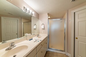 A bathroom with a double sink, a large mirror, and a shower stall.