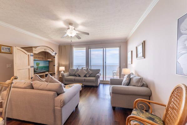 A spacious living room with a ceiling fan, a television, and a balcony with a view.
