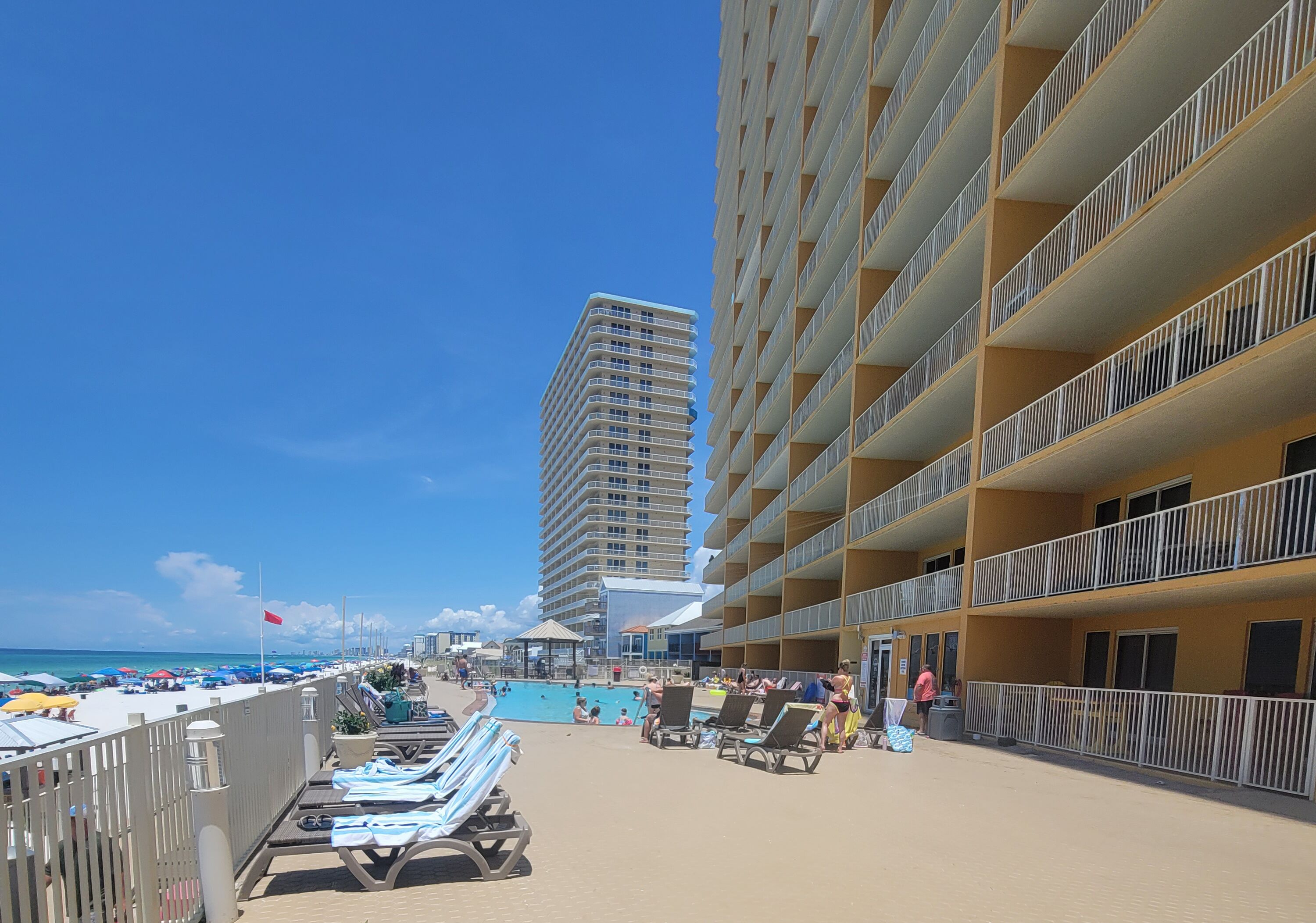 A beachfront hotel with multiple balconies, a pool area, and lounge chairs.