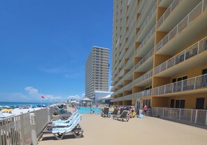 Un hotel frente a la playa con varios balcones, una zona de piscina y sillones de descanso.