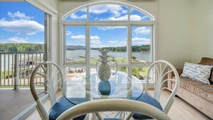 Una habitación con una mesa y sillas de vidrio, un sofá y un ventanal con vistas a un lago y vegetación.
