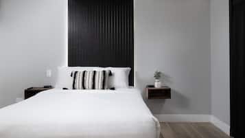 Une chambre moderne avec un grand lit, une table de chevet, une petite étagère avec une plante et un mur d’accent de couleur foncée.