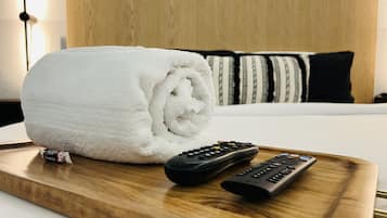 A neatly made white towel on a wooden tray, accompanied by two remote controls, in a hotel room setting.
