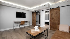 A modern living room with a wooden floor, a sofa, a coffee table, a TV mounted on the wall, and a sliding door closet. - The Cactus Cove Inn and Suites (Amarillo)