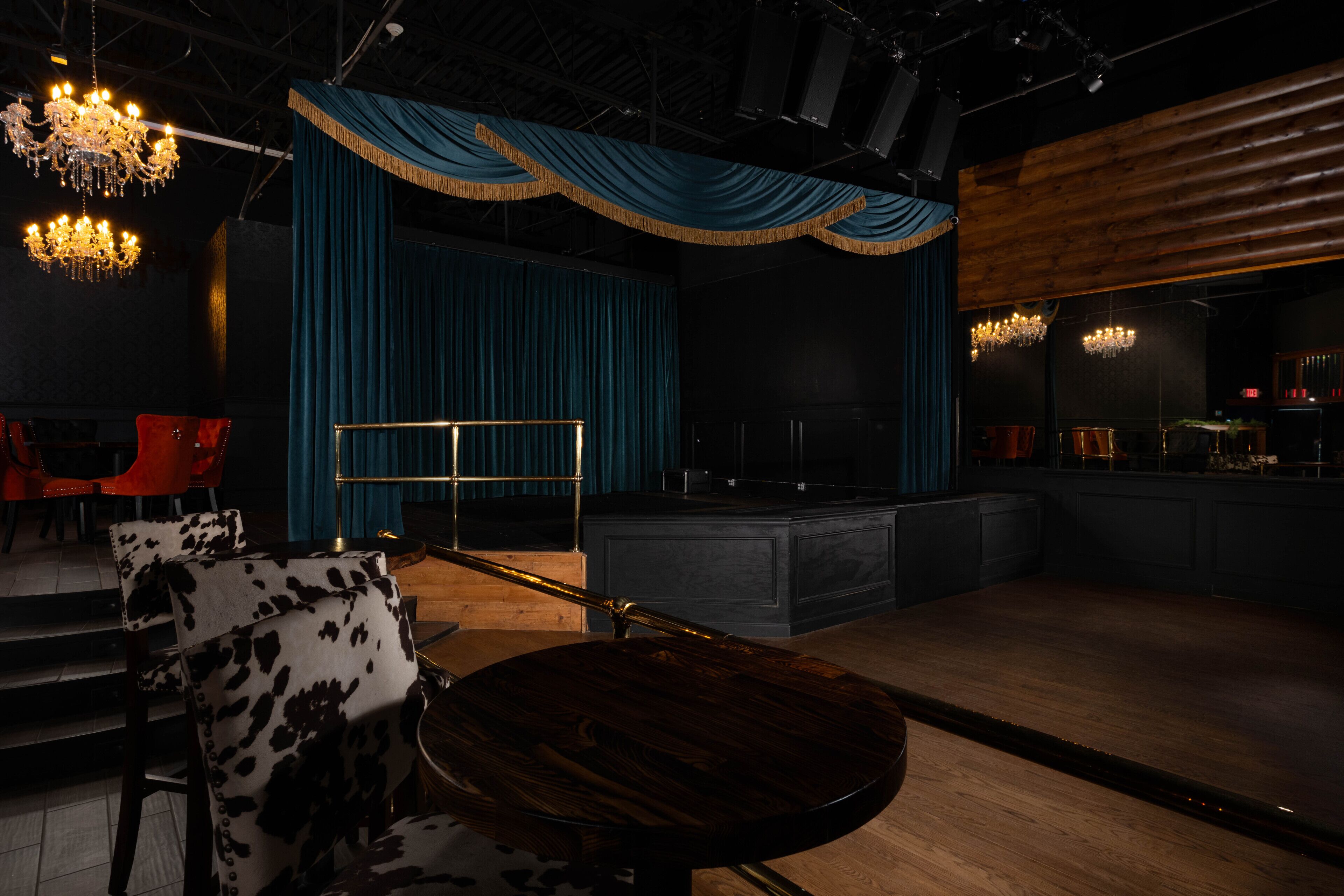 A stage with a blue curtain backdrop, a bar area with stools, and a chandelier.