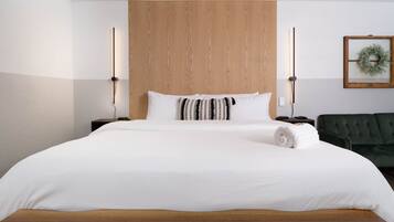 A hotel room with a large bed, wooden headboard, two bedside tables, a green sofa, and a wall-mounted wreath.