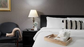 Habitación de hotel con cama, mesita de noche con lámpara, una silla y una bandeja con toallas.