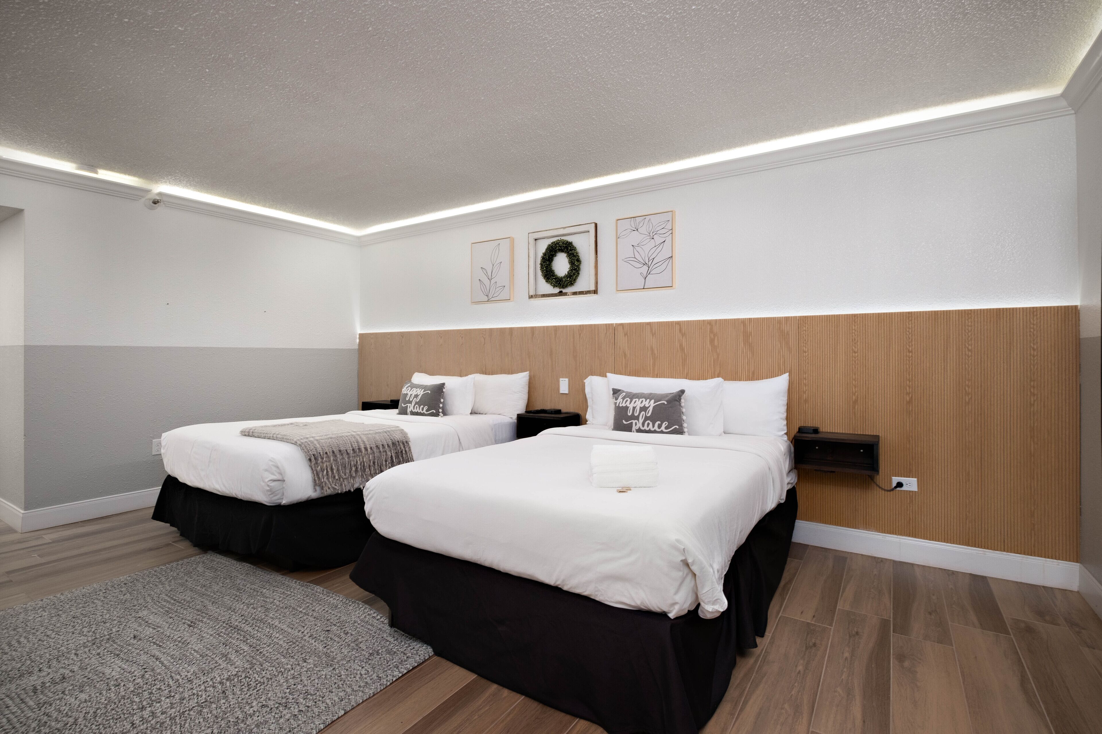 A hotel room with two beds, a wooden headboard, a gray rug, and a wall-mounted shelf.