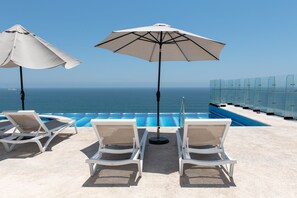 A poolside area with lounge chairs and umbrellas, overlooking a clear blue sea. - Tropicalisting (Mazatlán)