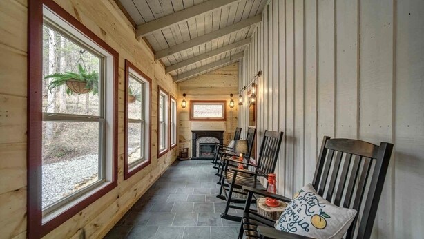 Una cabaña de madera con ventanas amplias, chimenea y varios sillones con cojines.