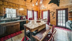 Interior rústico de una cabaña con paredes de madera, una mesa central también de madera, un sofá y un trofeo de piel de animal colgado.