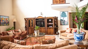 A spacious living room with a large sectional sofa, a glass coffee table, and a wooden entertainment center with a flat-screen TV.