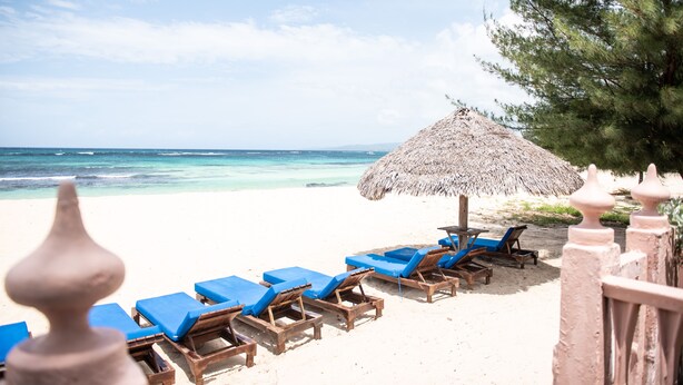 A beach with blue lounge chairs and a thatched umbrella.