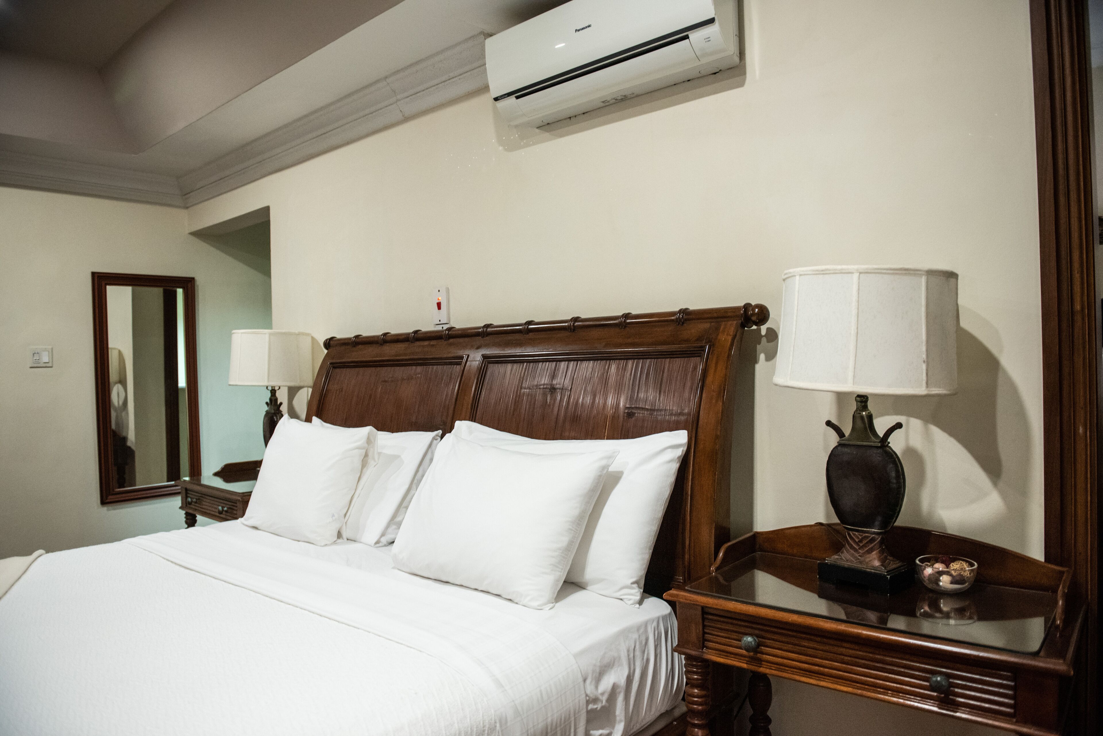A neatly made bed with white linens, a wooden headboard, and a bedside table with a lamp and decorative items.